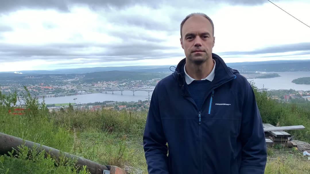 Man standing outside with a city in the background.
