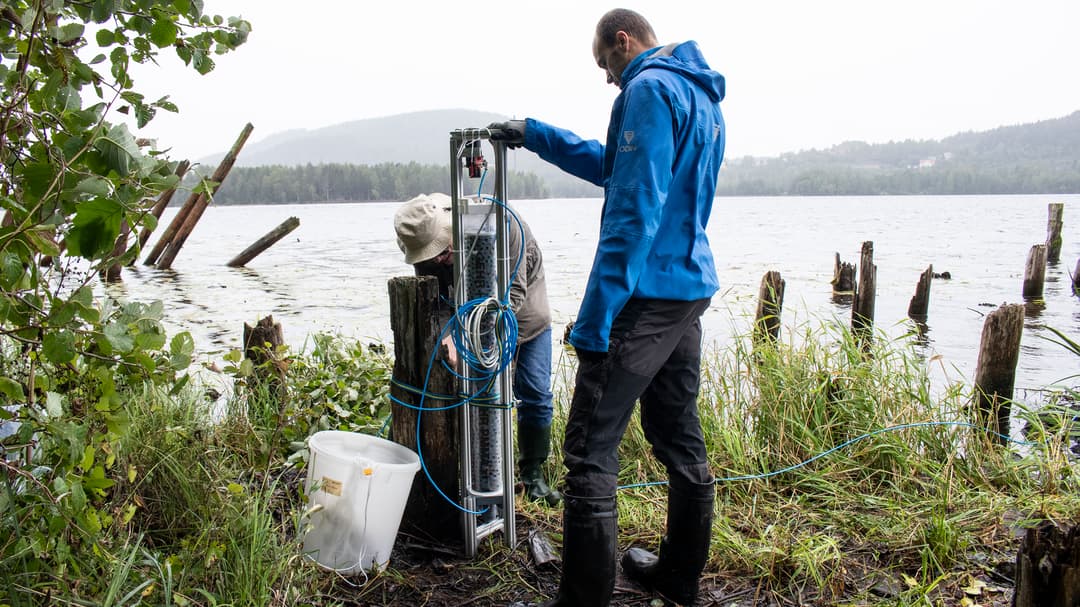 Two men stand and work with a demonstrator by water.
