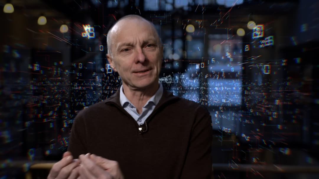 Man with light shirt and black knitted sweater in front of a digital background.