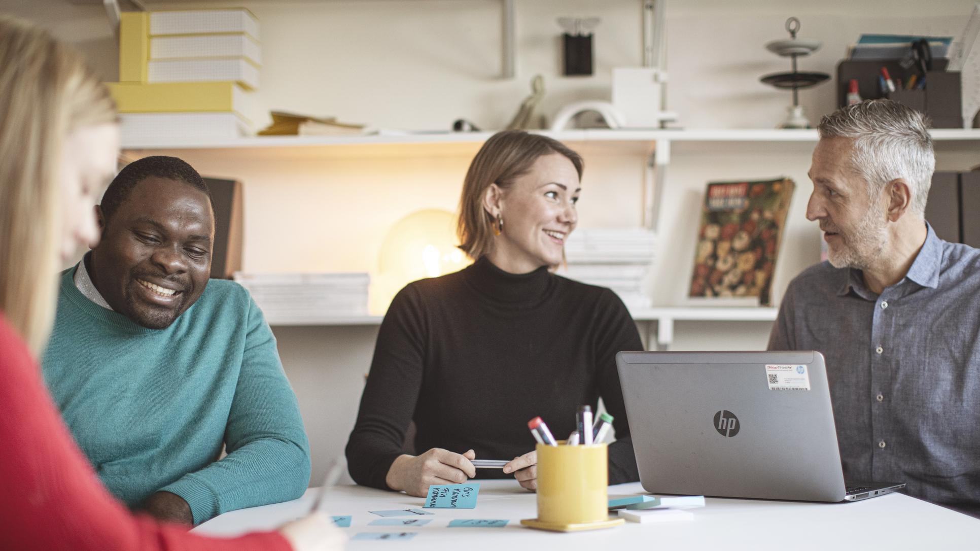 Fyra studenter runt ett bord som arbetar med en laptop och post-it lappar.