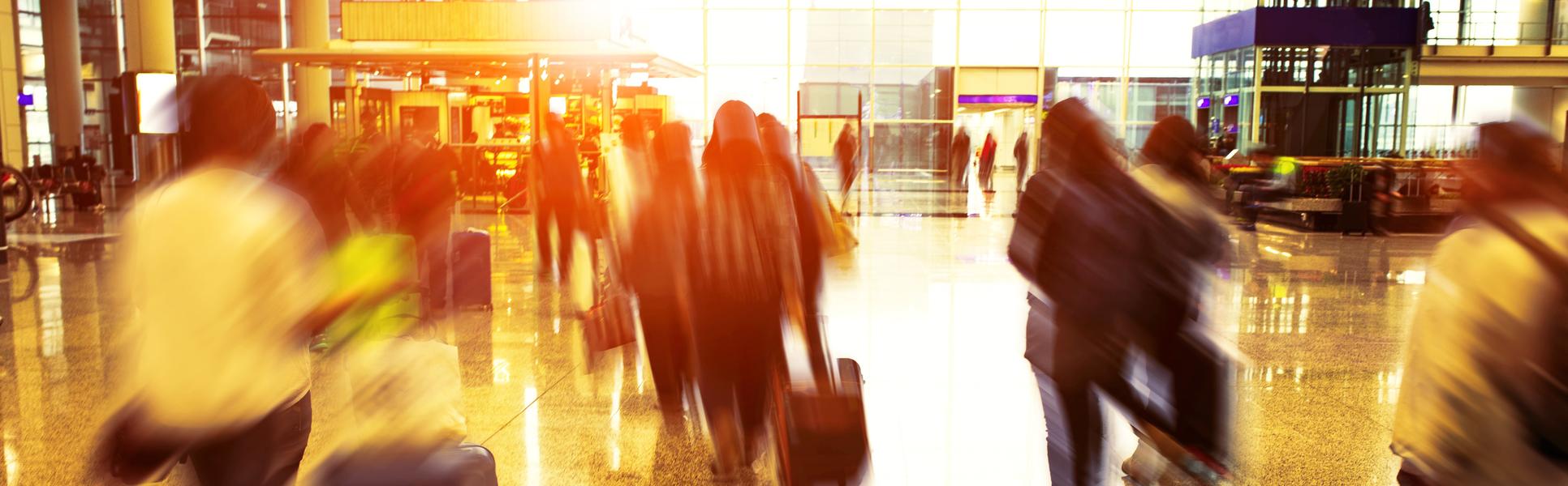 Människor går inomhus på flygplats med resväskor och ett flygplan syns genom fönstret utanför 