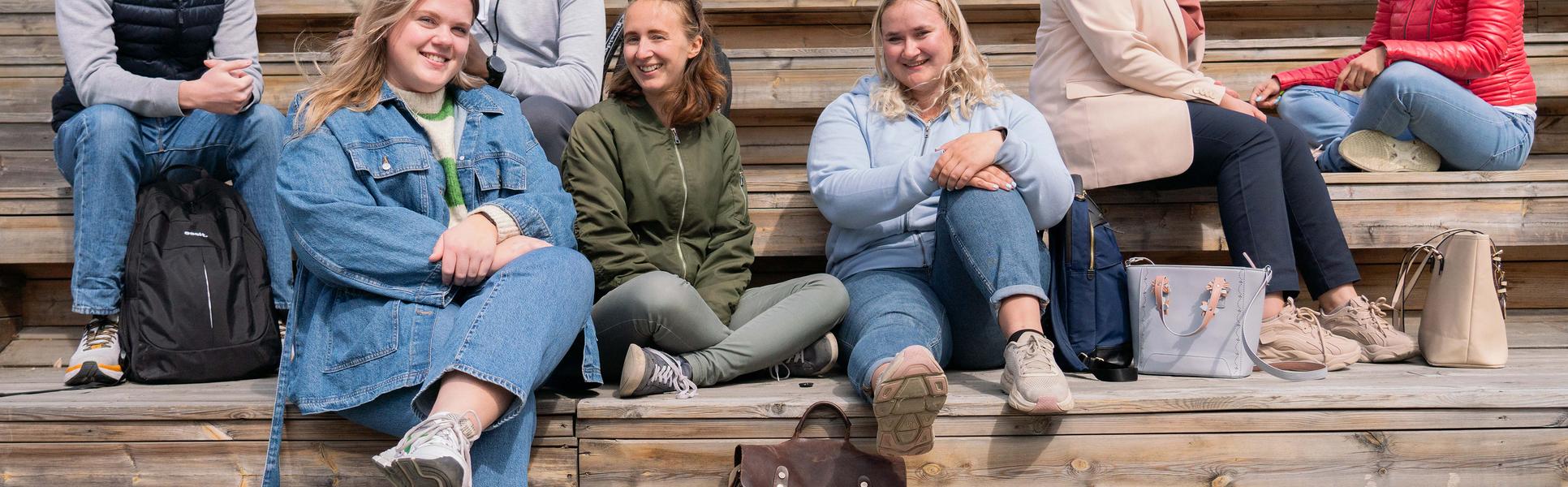 En grupp studenter sitter i en trätrappa och pratar.