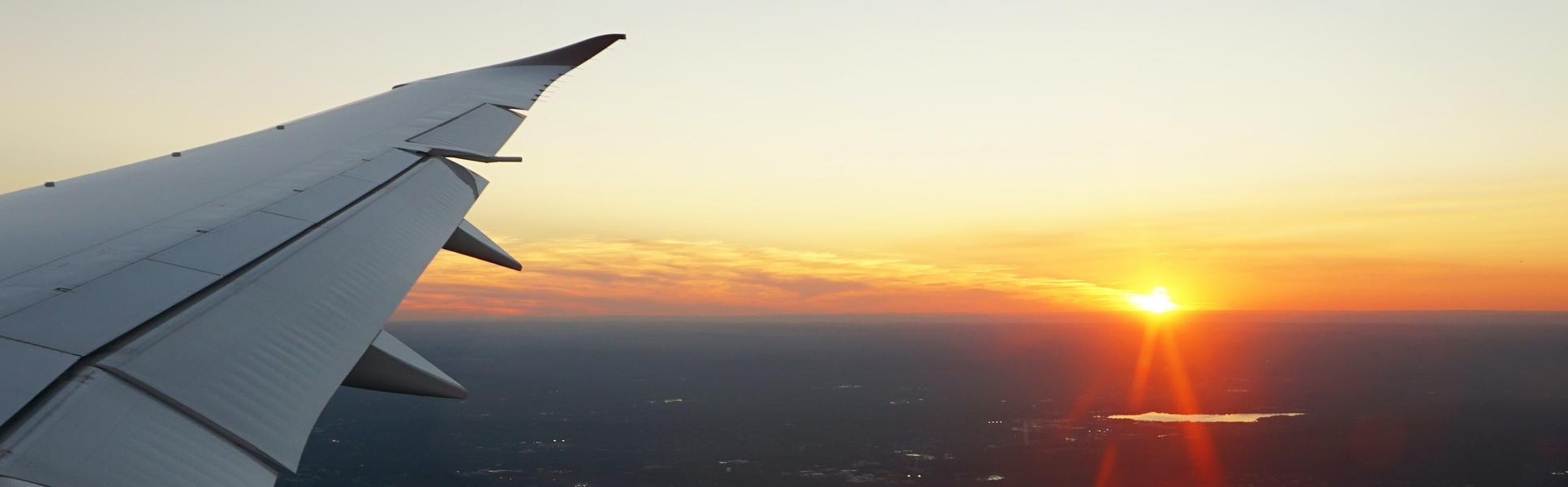 Flygplansvinge och solnedgång genom ett flygplansfönster