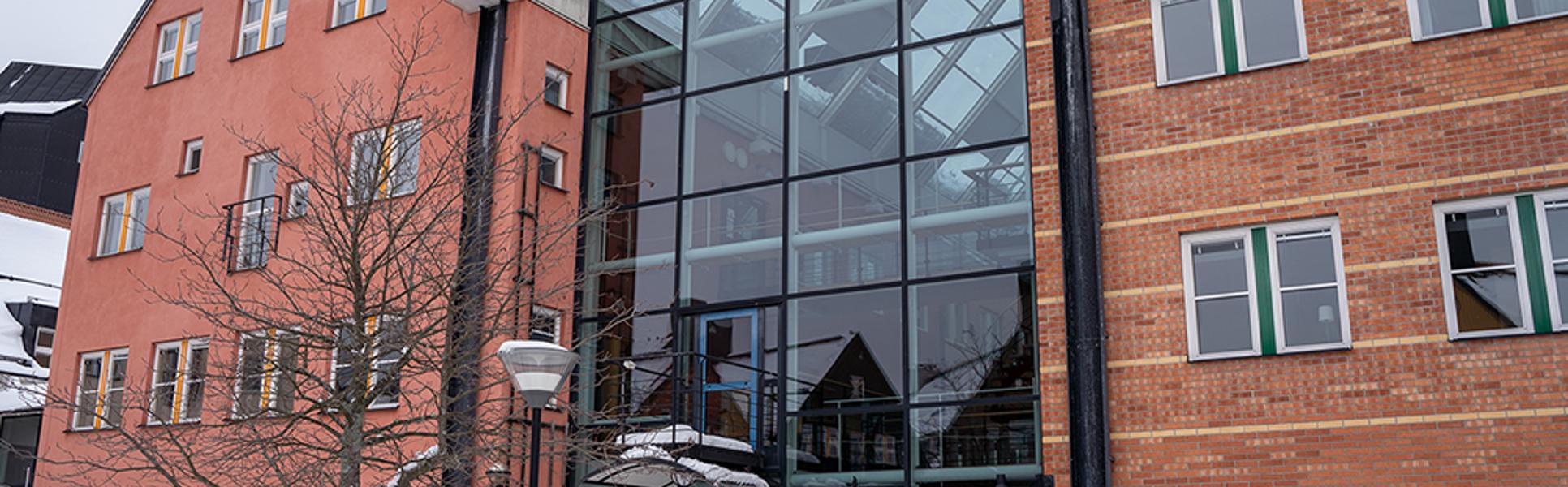 Röda byggnader ihoplänkade med en glasbyggnad.