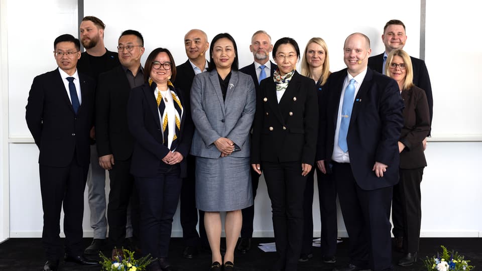Gruppfoto av män och kvinnor i kostym/dräkt framför vit vägg