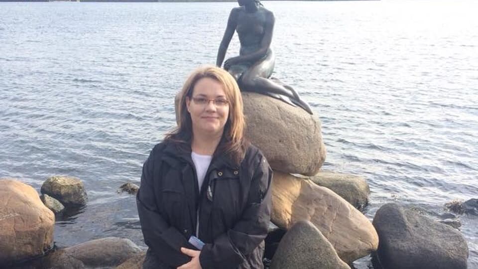 En kvinna står på en sten framför statyn "Den lilla sjöjungfrun" i Köpenhamn. 