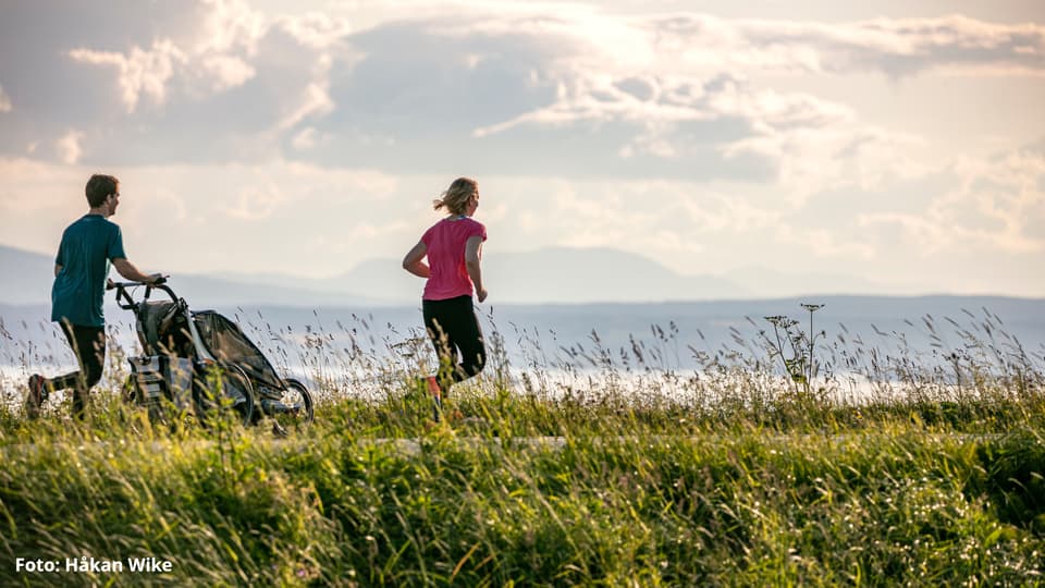 Ett par springer med en Thule-vagn längs med Storsjön