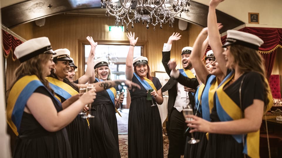 En grupp glada ungdomar med studentmössor jublar med en hand i luften.