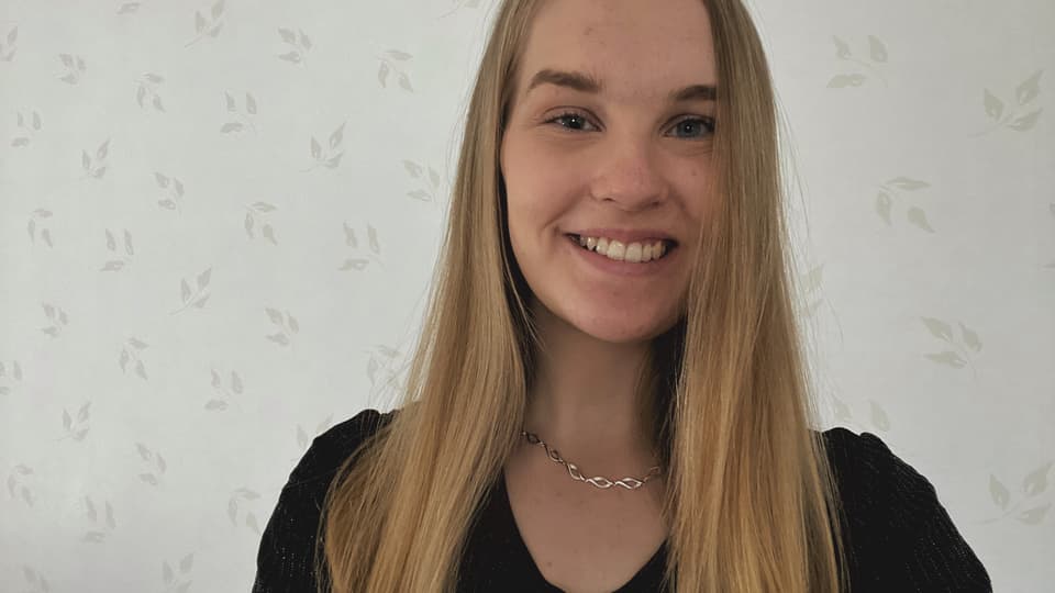 Light-haired woman in front of a light but patterned wallpaper