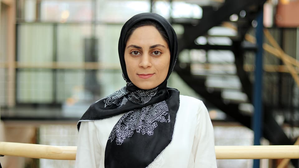 Woman in white sweater and black, white-patterned headscarf.