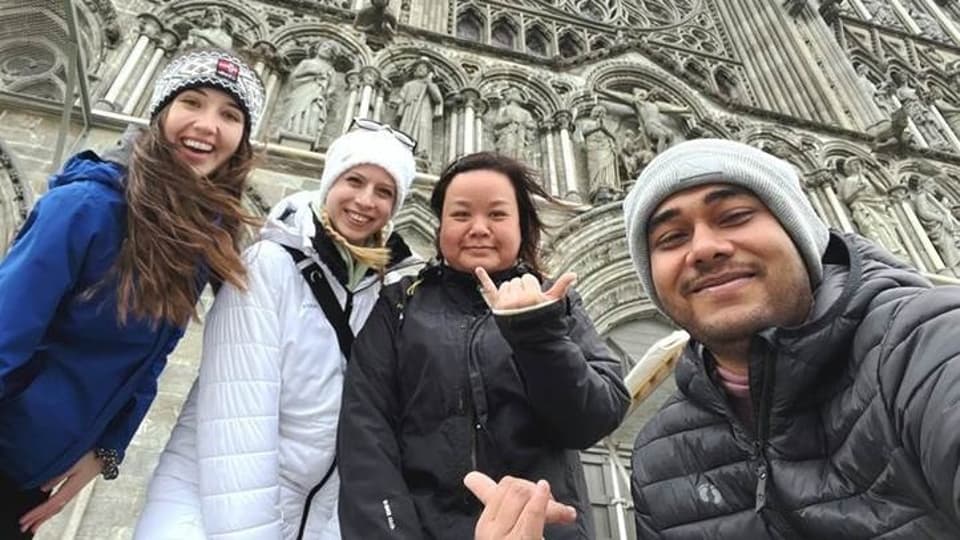 Fyra glada, unga människor står framför en kyrka iklädda ytterkläder. 