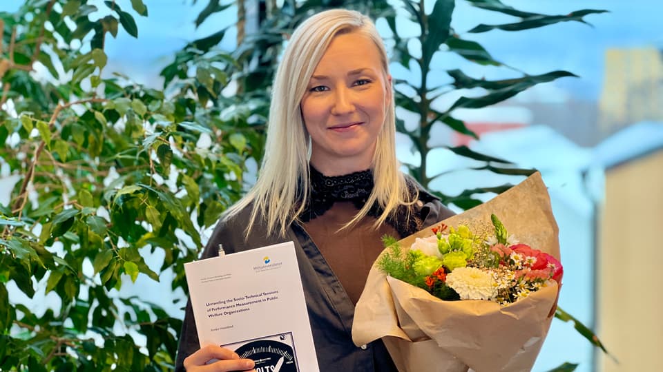 En blond kvinna håller i en bok och blommor