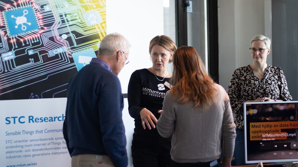 Two women standing and talking to two people. A rollup with the text STC Research next to them. 