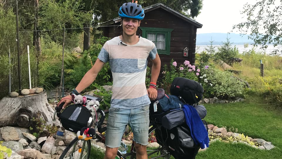 Ung man står vid fullpackad cykel.