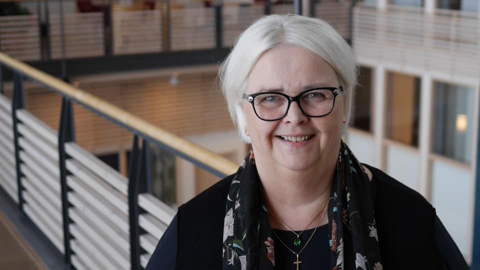 Kvinna står i ljushallen på Mittuniversitetet campus Östersund. Hon tittar in i kameran och ser glad ut.