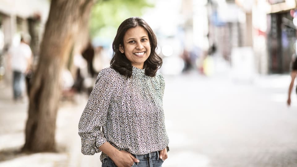 Kvinna i mönstrad blus och jeans ler mot kameran