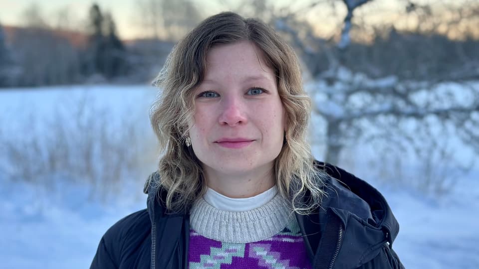 Kvinna med axellångt hår och jacka i förgrunden och ett vinterlandskap i bakgrunden