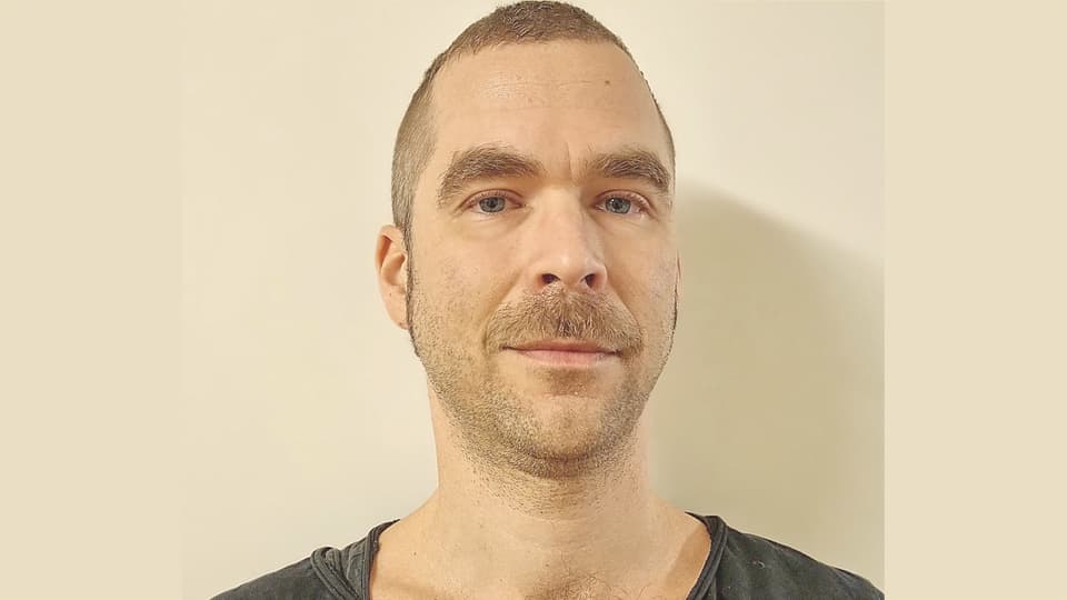 En man med snaggat brunt hår och svart t-shirt