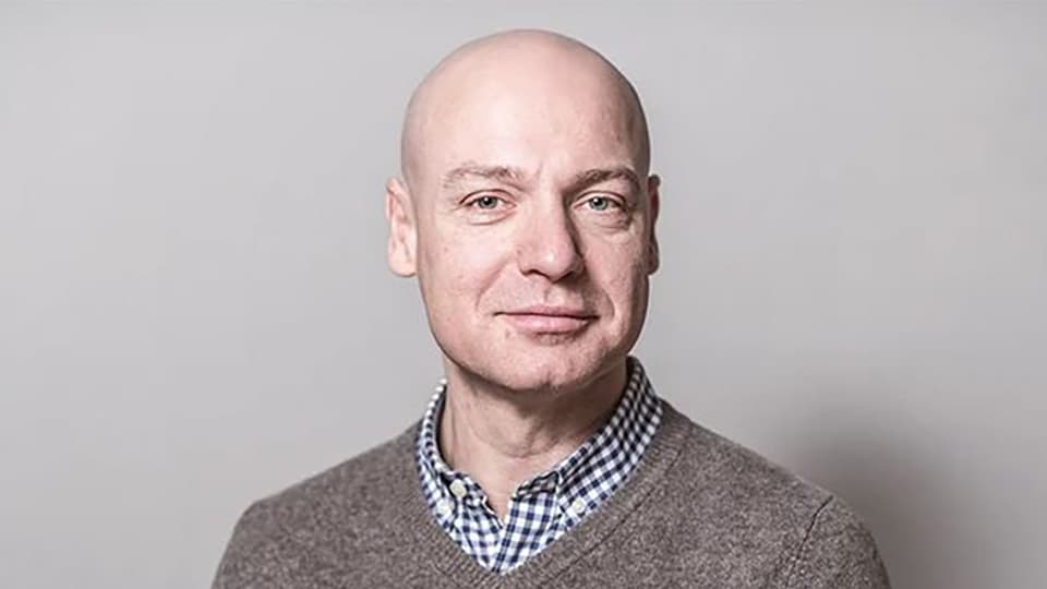 Ett porträttfoto av en man med rakat huvud och grå tröja