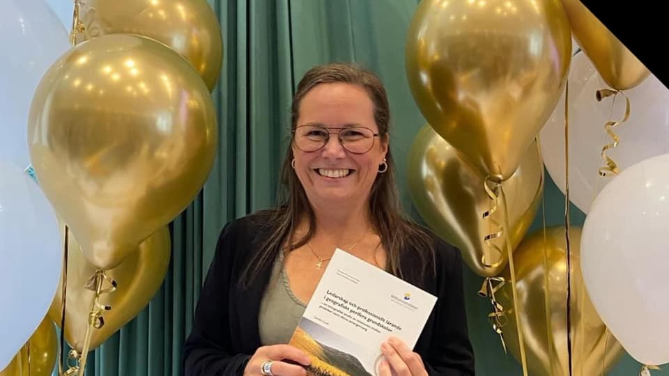Sandra Lund står med sin avhandling framför en grön duk med ballonger på sidan om