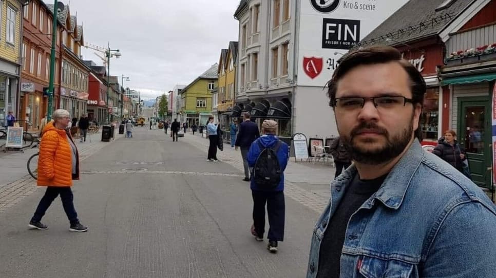 Joakim Pettersson står på en gata och tittar in i kameran. Andra människor och byggnader syns i bakgrunden.
