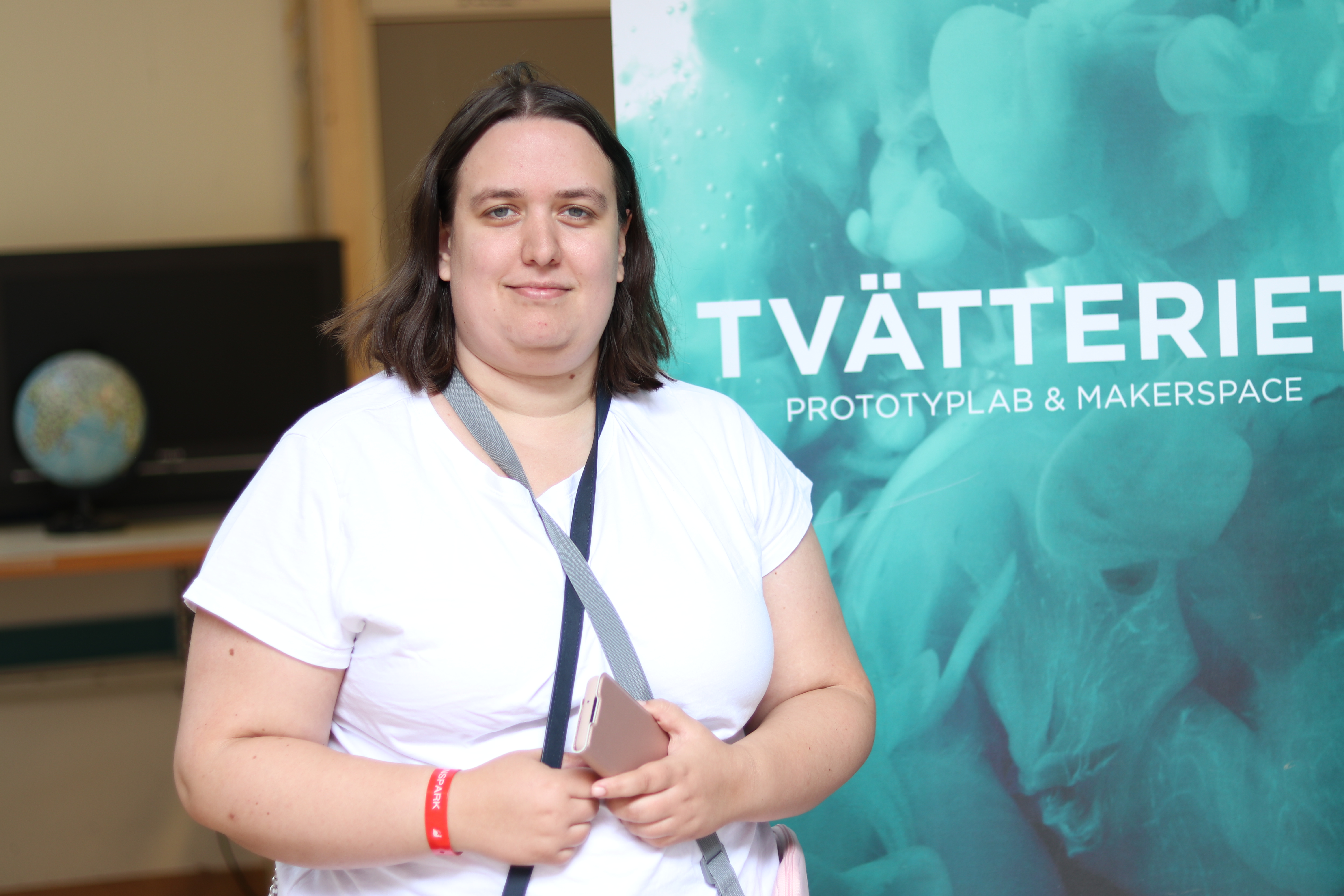 Woman in white t-shirt stands in front of a blue rollup with the text “TVÄTTERIET