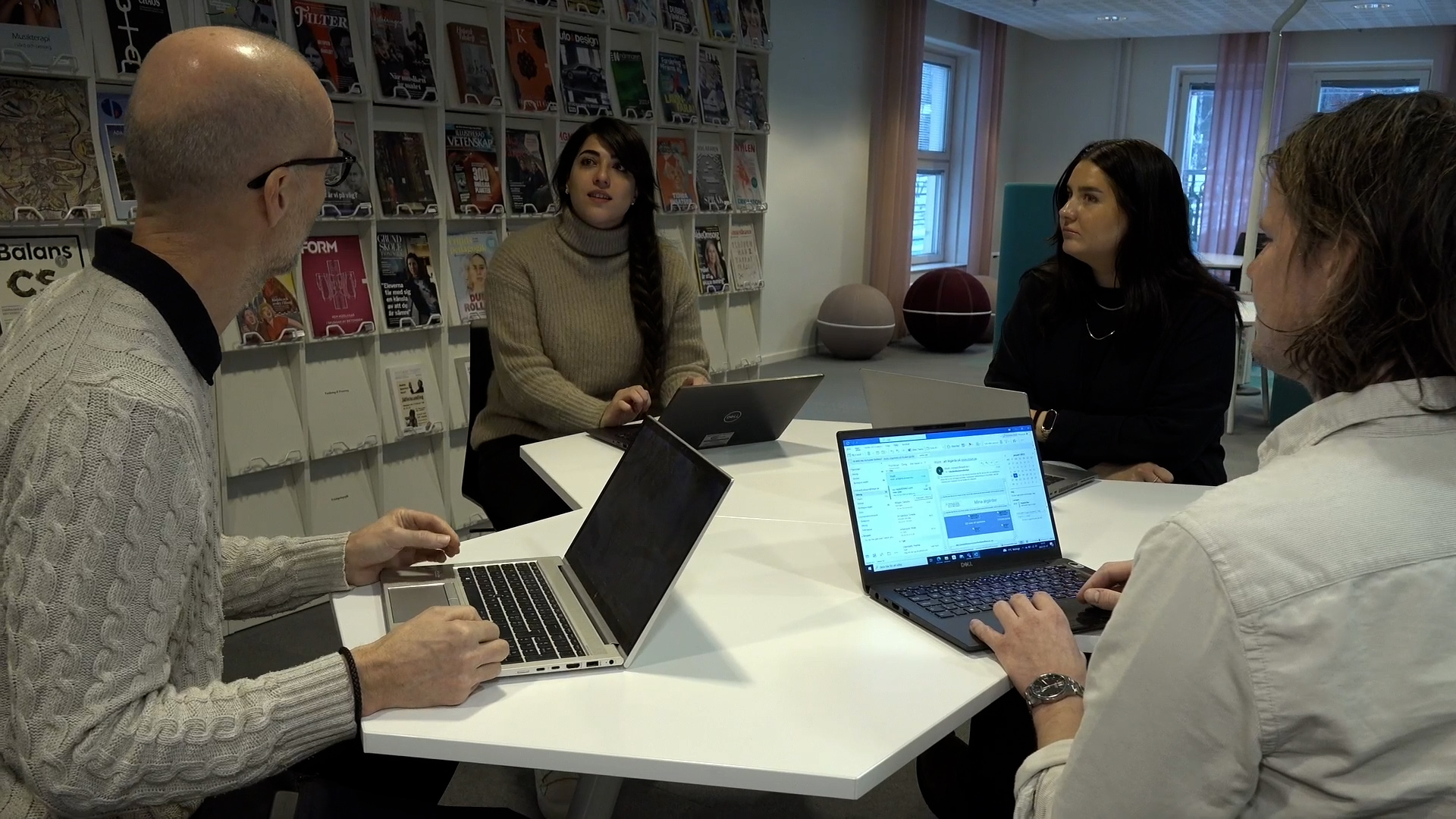 Four people, each with a laptop, are sitting at a table and talking.