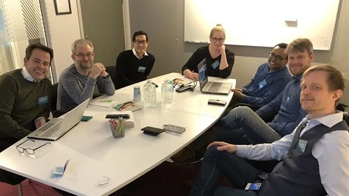 Seven people sitting around a table discussing a topic during Business Innovation Day.