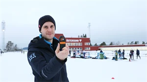 Man showing off a sensor standing outdoors in a biathlon stadium in winter landscape.