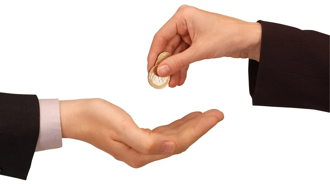 En hand släpper mynt i en annan hand. Pengar byter ägare.