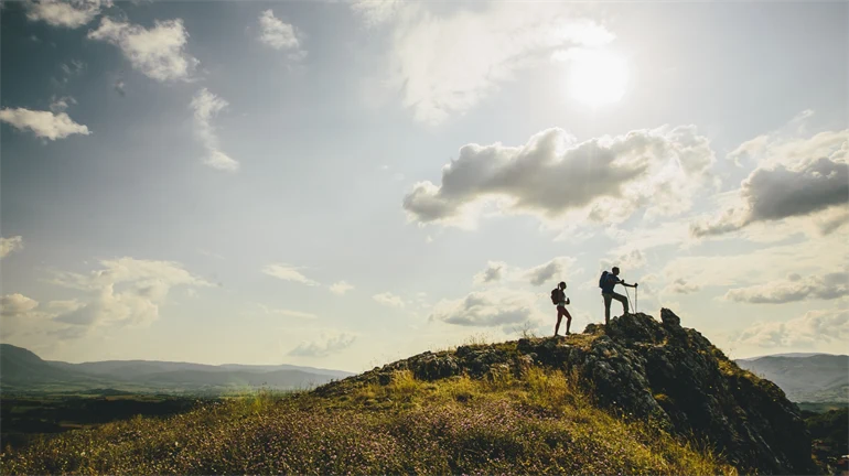 Man och kvinna med ryggsäck och stavar blickar ut över fjälllandskap