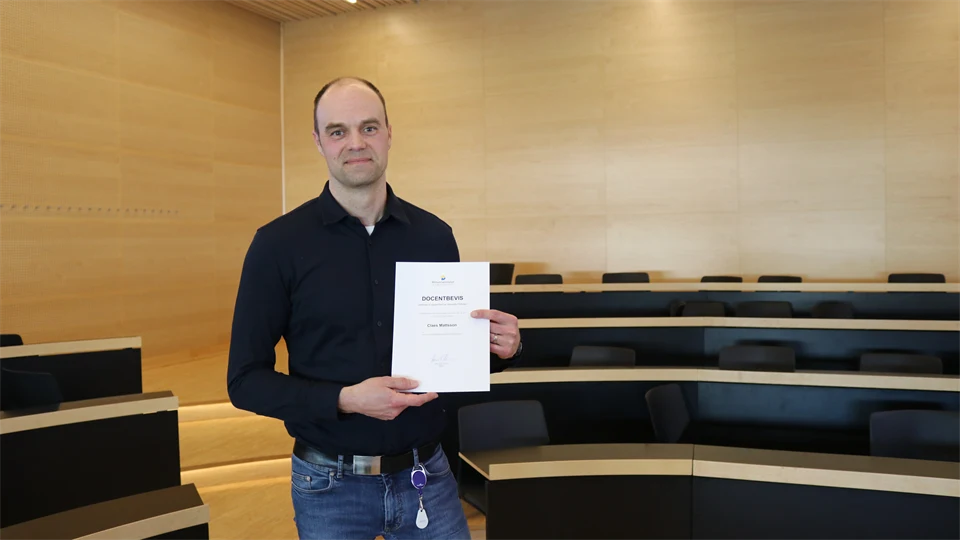 En person står och visar upp ett docentbevis