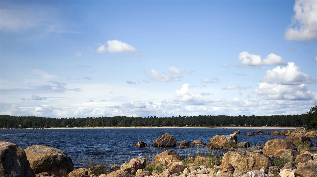 Bild på vatten, blå himmel och en stenstrand 