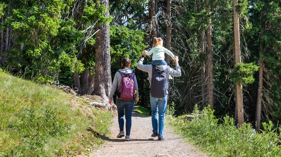 kvinna med ryggsäck  och man med barn på axlarna vandrar i skogen