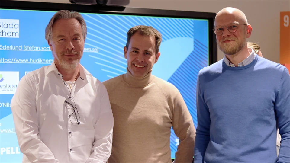 Tre män står framför en stor tv-skärm.