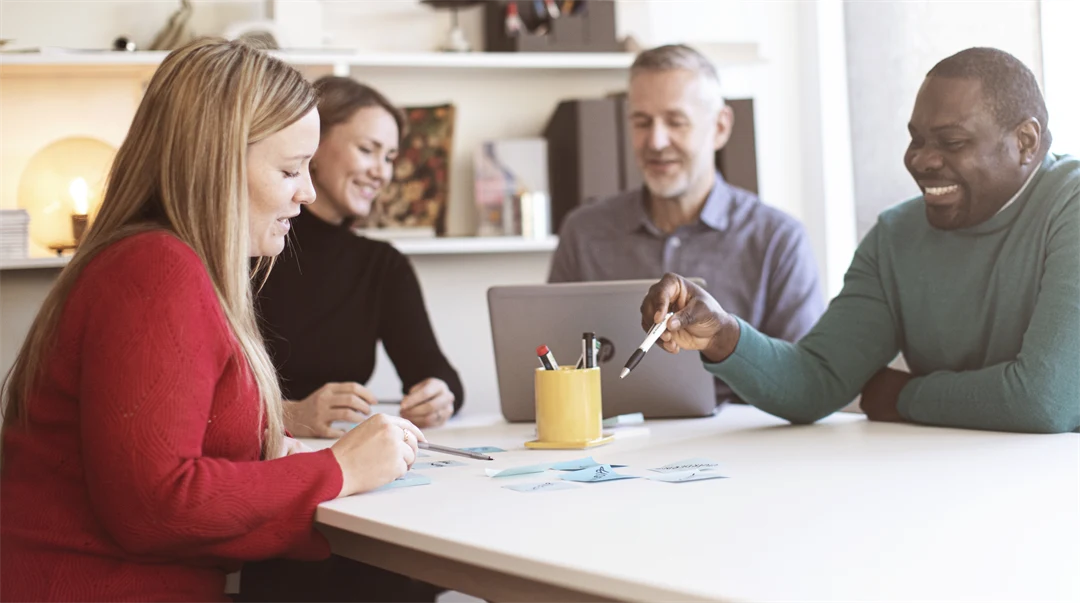 Fyra studenter runt ett bord som arbetar med en laptop och post-it lappar.
