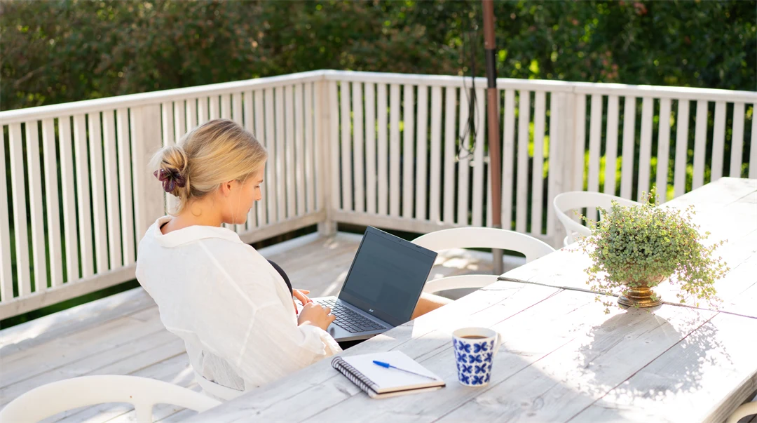 Kvinna som sitter vid ett bord på altan med laptop och pluggar.