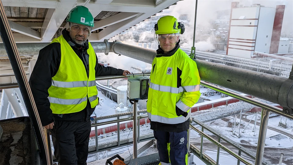 Två män i varselkläder i ett vintrigt industrilandskap.