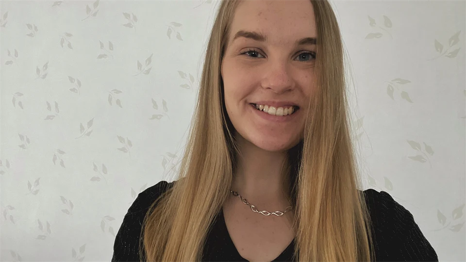 Ljushårig kvinna framför en ljus men mönstrad tapet