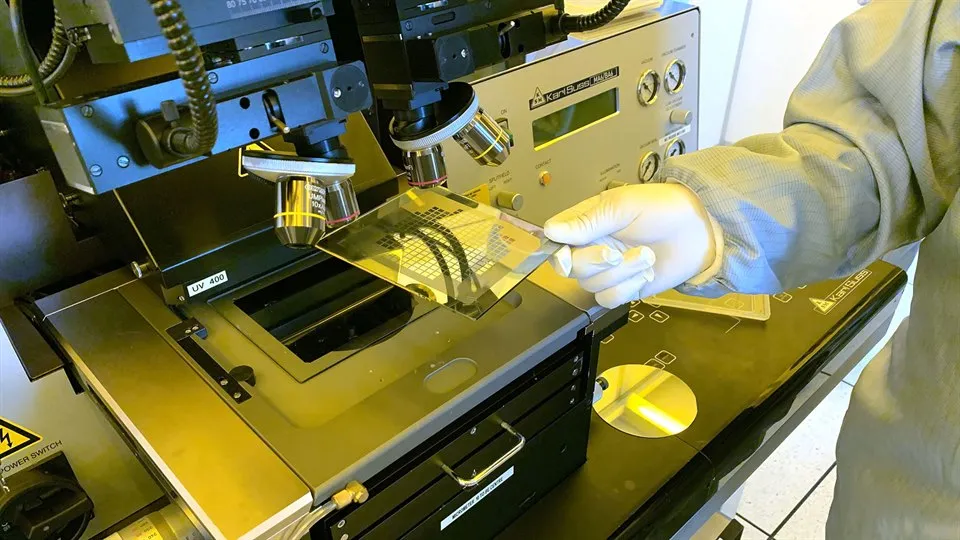 Hand håller en fyrkantig platta under ett mikroskåp.