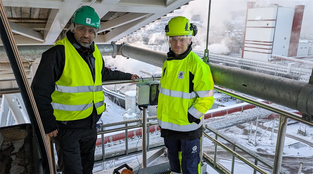 Två män i varselkläder i ett vintrigt industrilandskap.