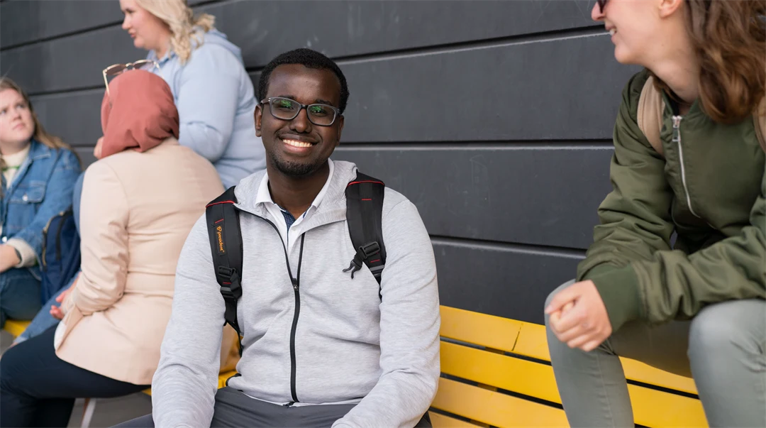 Två studenter som sitter på gul bänk och pratar med varandra.