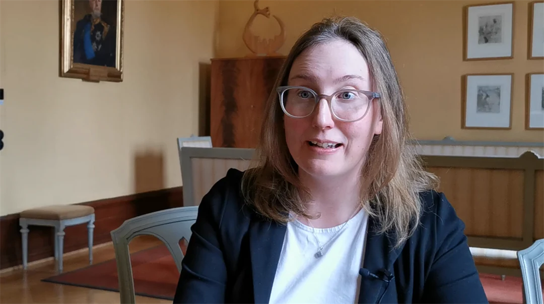 Kvinna med brunt axelångt hår klädd i svart kavaj blir intervjuad