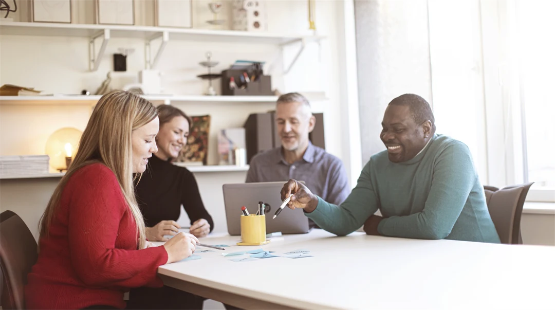 Fyra studenter runt ett bord som arbetar med en laptop och post-it lappar.