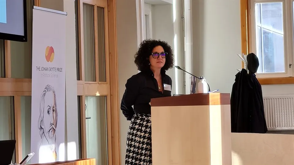 En kvinna står vid ett podium i en föreläsningssal. 