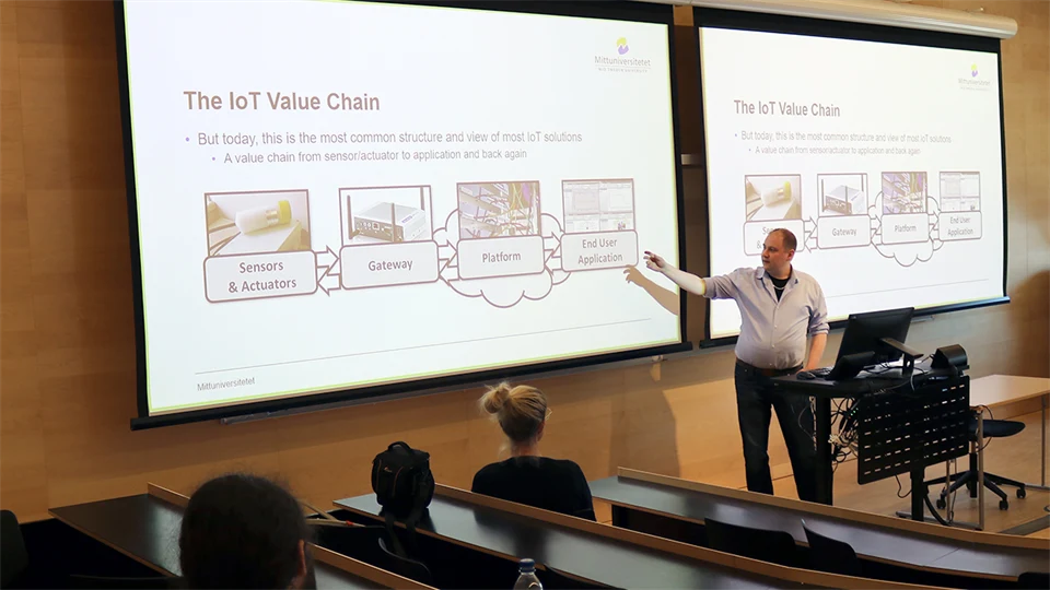 En man i en ljusblå skjorta står framför en stor skärm och håller en presentation.