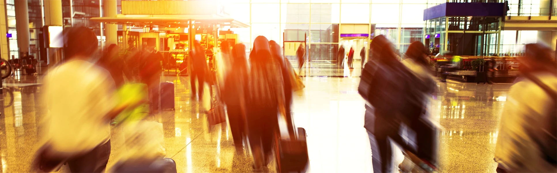 People walk indoors in airport with suitcases and an airplane is visible through the window outside