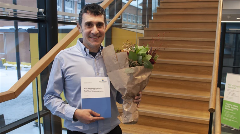 En mörkhårig man poserar för kameran med en blombukett och sin doktorsavhandling.