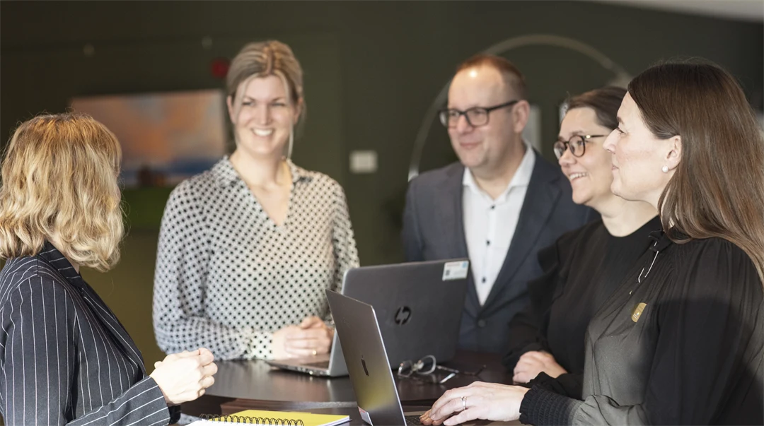 Fem personer står vid ett ståbord och diskuterar något