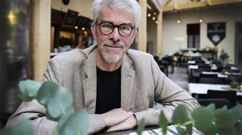 En man med vitt hår och glasögon som sitter vid ett bord